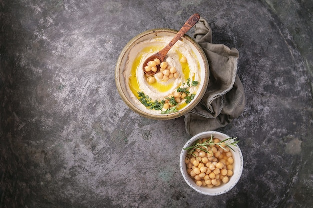 Bol à houmous fait maison, décoré de pois chiches bouillis, d'herbes et d'huile d'olive sur un fond en métal rustique. Vue de dessus.