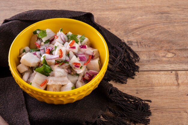 Un bol jaune avec ceviche sur une table en bois.