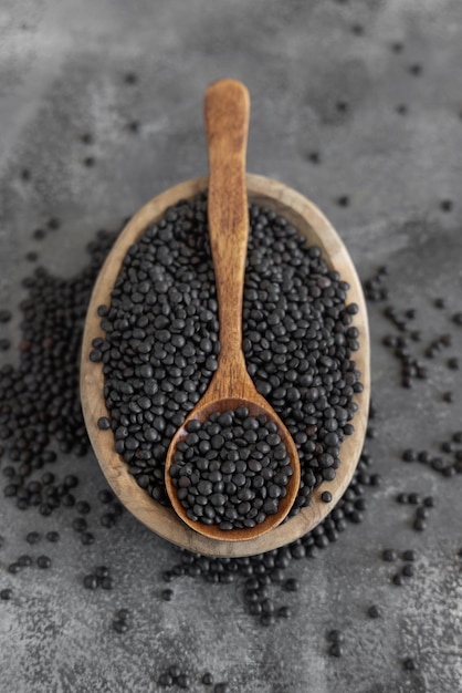 Bol de lentilles noires sèches avec une cuillère sur une table grise close up source de protéines pour le régime végétarien