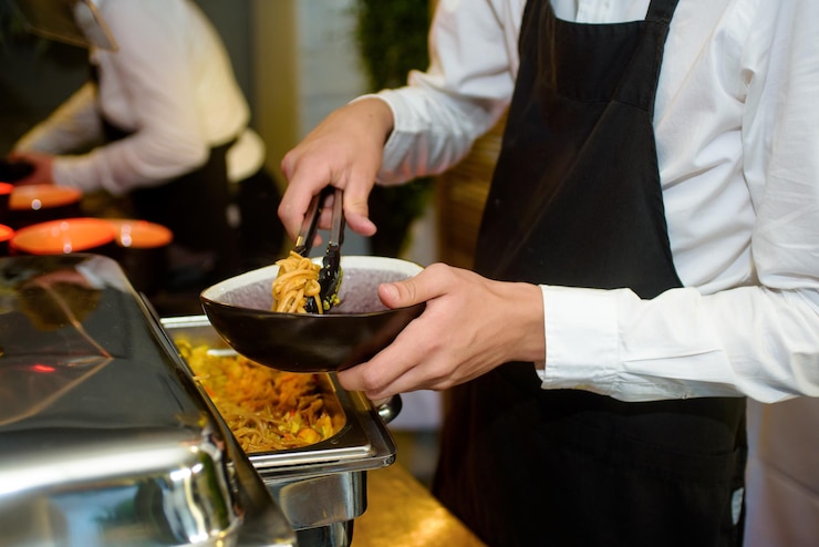 Photo un bol noir avec des nouilles servi à une fête par un serveur avec un tablier de cuisine noir