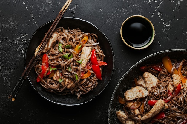 Bol avec des nouilles soba sautées au poulet asiatique avec des légumes sur fond de pierre noire foncée d'en haut, plat de nouilles chinoises thaïlandaises ou japonaises avec sauce soja