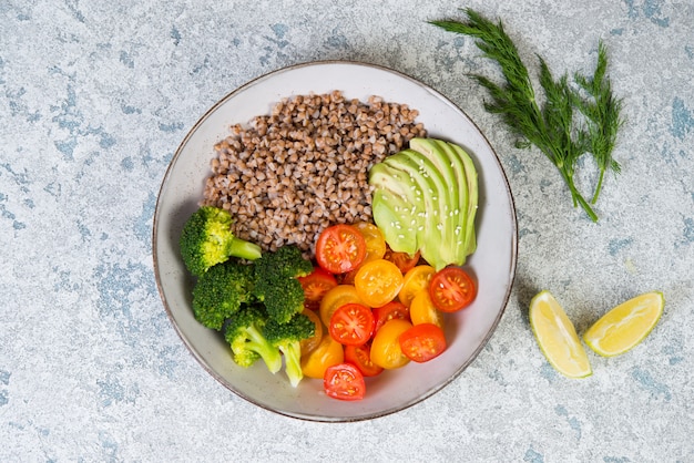 Un bol de nourriture végétalienne, un dîner végétalien de sarrasin bouilli, de tomates colorées, d'avocat et de brocoli. Vue de dessus