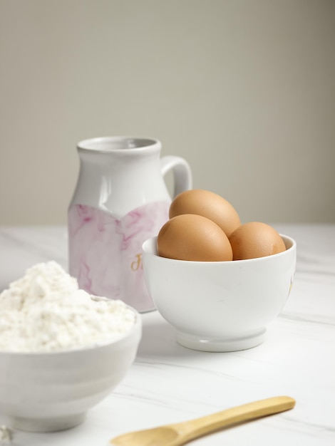 Un bol d'œufs avec de la farine de blé et du lait en arrière-plan. Concept de préparation de cuisson