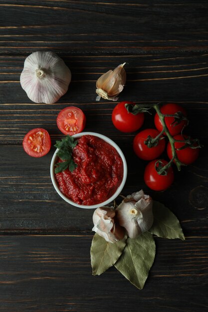 Bol avec pâte de tomates, tomates et ail sur table en bois