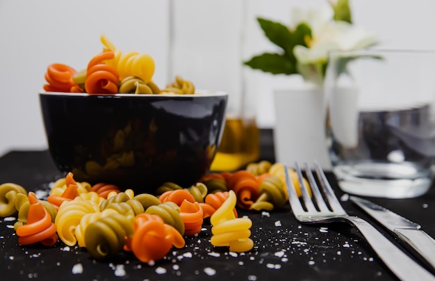 Un bol de pâtes avec une fourchette et un verre de fleurs blanches sur la table.