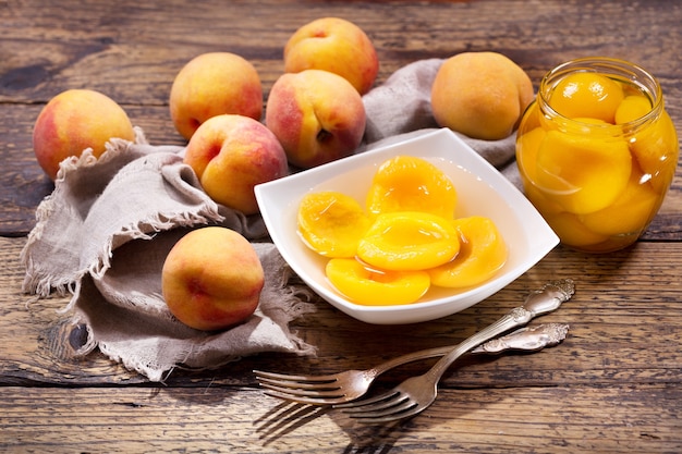 Bol de pêches en conserve avec des fruits frais sur table en bois