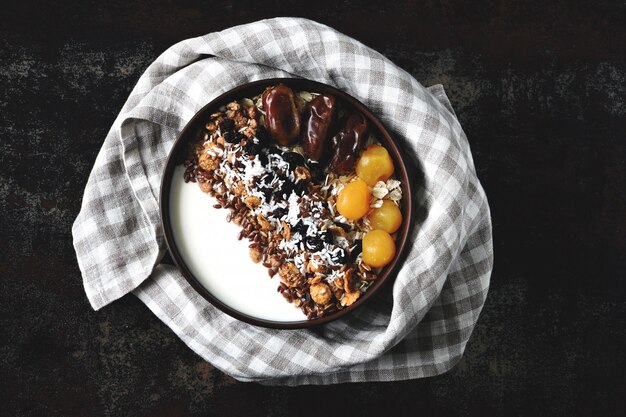 Bol de petit déjeuner avec du yaourt grec, de la farine d'avoine, du granola et des fruits secs.