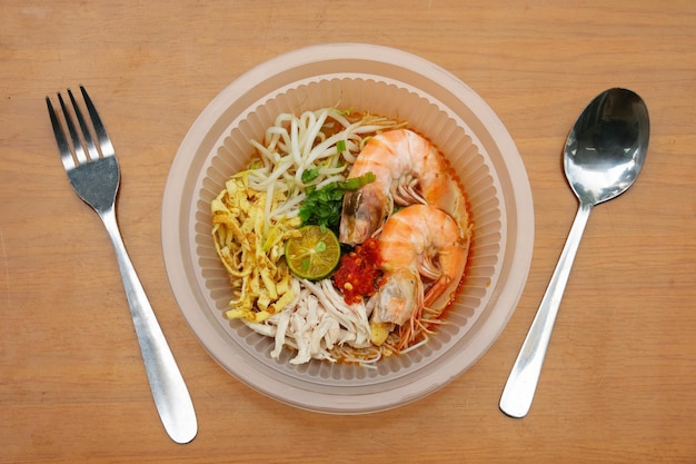 Photo un bol photo de laksa sarawak avec une fourchette et une cuillère sur la table composé de vermicelles crevettes soupe de noix de coco sauce poulet et œufs