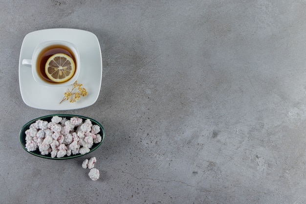 Un Bol Plein De Bonbons Blancs Sucrés Avec Une Tasse En Verre De Thé Chaud Sur Une Pierre