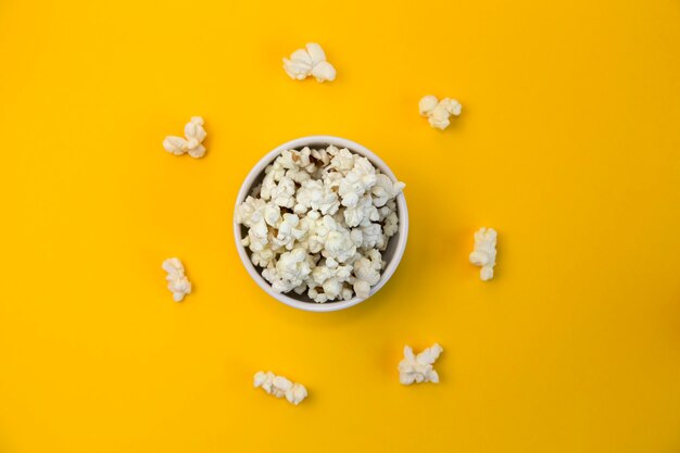 Bol plein de pop-corn sur fond jaune et pop-corn autour du bol. Regardez des films amusants.