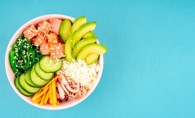 Un bol poke suspendu, salade de poisson cru, d'algues, de riz, de saumon, de concombre, de sauce soja, d'avocat et de graines de sésame.