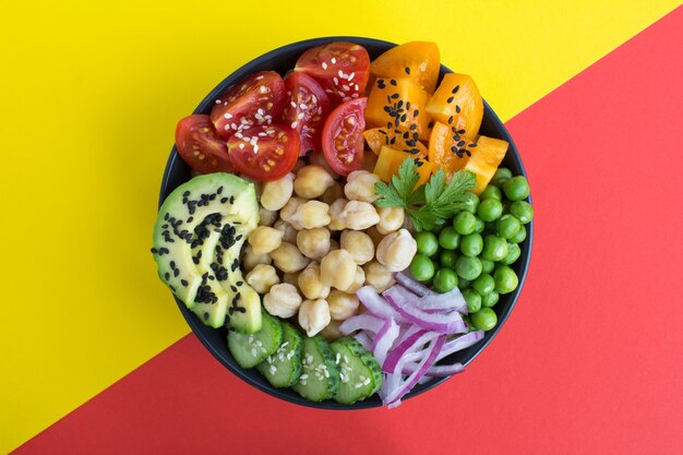 Bol poke vegan avec pois chiches et légumes dans le bol noir au centre de l'arrière-plan coloré.Vue de dessus.Gros plan.