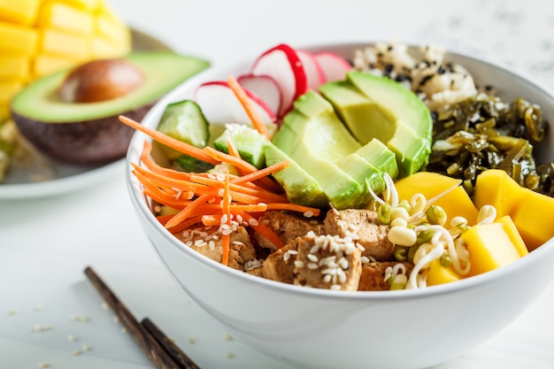 Bol poke végétalien avec avocat, tofu, riz, algues, carottes et mangue. Concept de nourriture végétalienne.