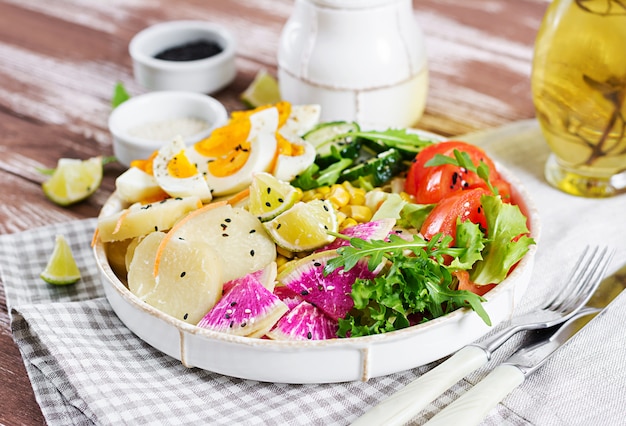 Bol avec pomme de terre bouillie, concombre, tomate, radis pastèque, laitue, roquette, maïs et œuf à la coque.