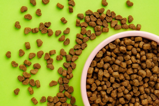 Un bol pour animaux de compagnie avec de la nourriture sèche sur fond vert, prise de vue en studio