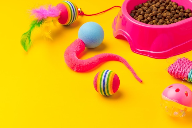 Un bol pour chat avec de la nourriture sèche et des jouets sur fond jaune.