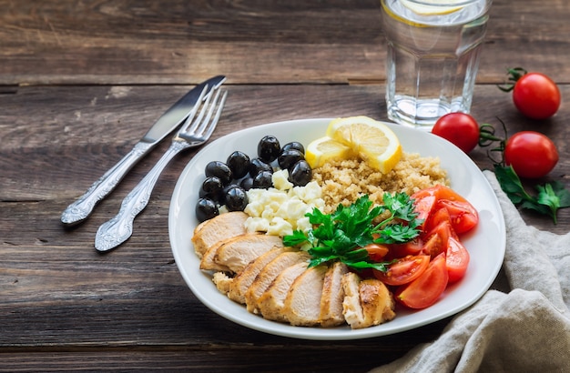 Bol de quinoa au poulet sain avec tomates cerises, feta, olives et persil sur table en bois rustique.