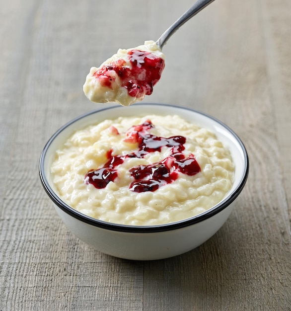 Bol de riz au lait décoré de confiture de baies sauvages sur une table de cuisine en bois