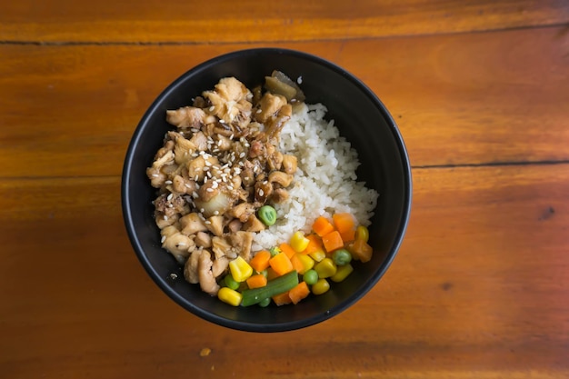 Bol de riz au poulet teriyaki avec légumes et maïs sur fond de bois