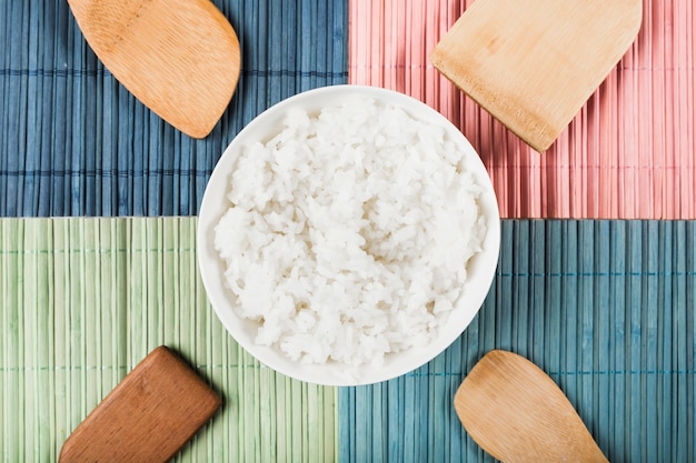 Bol de riz cuit à la vapeur blanc avec un type différent de spatule en bois sur un napperon coloré