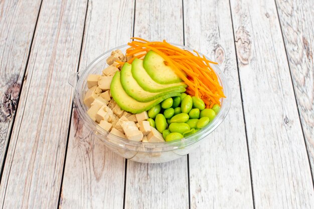 Bol sain de tofu insipide avec des tranches d'avocat mûr zeste de carotte haricots edamame base de riz blanc à l'intérieur d'un bol transparent pour la livraison à domicile