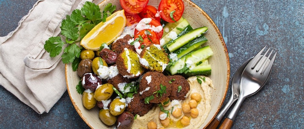 Un bol de salade de falafel avec du houmous, des légumes, des olives et des herbes