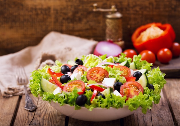 Bol de salade fraîche avec des légumes et des verts sur table en bois