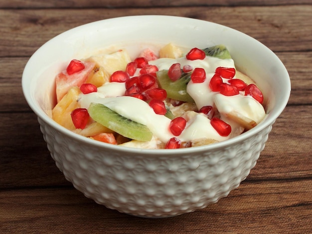 Bol de salade de fruits frais sains avec de la crème servi sur un fond en bois rustique mise au point sélective