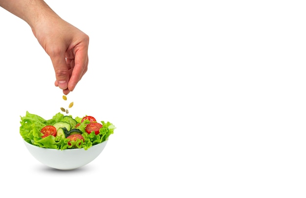 Un bol de salade et un mâle saupoudrant des graines sur la salade isolée