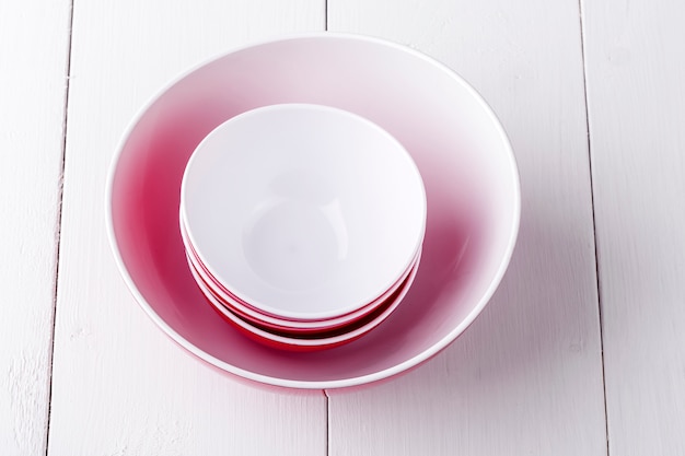 Un bol à salade rouge vide et des tasses sur une table en bois blanc