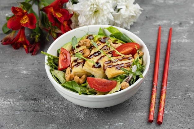 Un bol de salade de tofu avec une paire de baguettes à côté