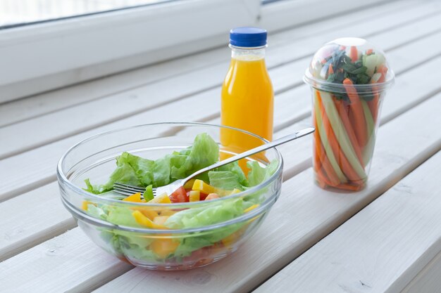 Bol de salade verte, crudités et bouteille de jus d'orange. Perte de poids, régime et droit