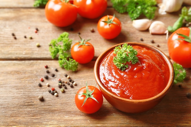 Bol avec sauce, tomates, verdure et épices sur table en bois