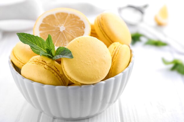 Bol avec de savoureux macarons au citron sur une table en bois blanc agrandi