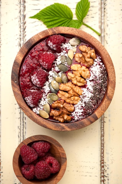 Bol de smoothie aux framboises, graines de chia, graines de citrouille et noix sur fond rustique