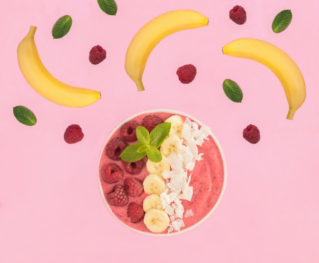 Photo un bol de smoothie avec des framboises, des bananes et des chips de noix de coco sur le fond rose vue supérieure en gros plan