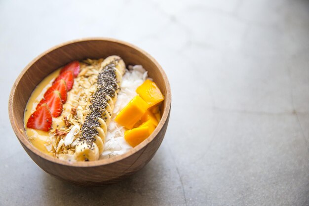 Bol De Smoothie à La Mangue Avec Fraise, Banane, Noix De Coco Et Flocons D'avoine Sur Fond De Béton. Concept D'alimentation Saine.