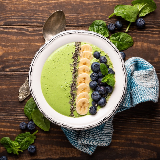 Bol de smoothie vert de désintoxication petit déjeuner de banane et d'épinards sur une surface en bois