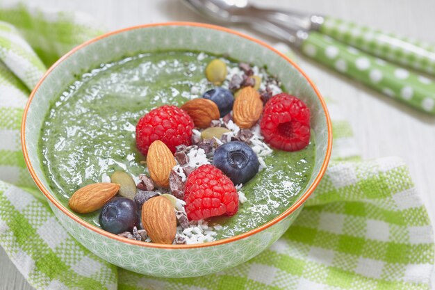 Bol de smoothie vert avec garniture de baies, noix et graines