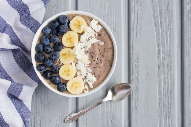 Bol de smoothies aux bleuets, bananes et chips de noix de coco sur le fond en bois gris. Vue de dessus. Espace de copie.