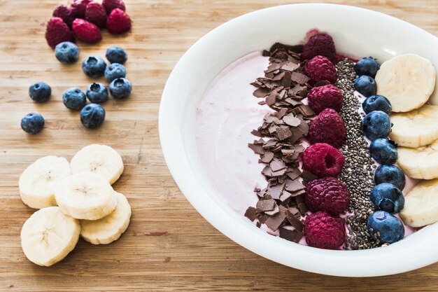 Bol à smoothies avec des baies fraîches, des bananes, des graines de chia et du chocolat