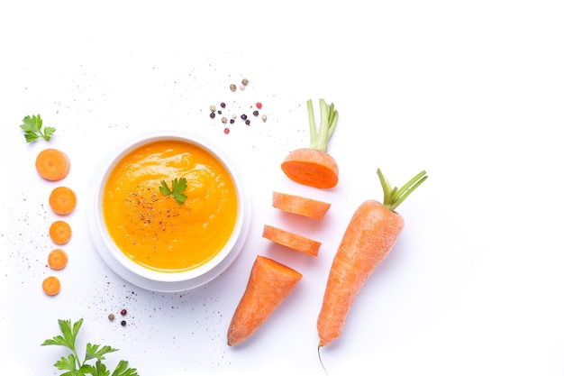 Bol de soupe aux carottes avec des morceaux de carottes isolé sur fond blanc