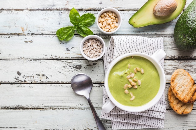 Bol de soupe à la crème de brocoli et pois verts dans un bol blanc avec avocat, vue de dessus