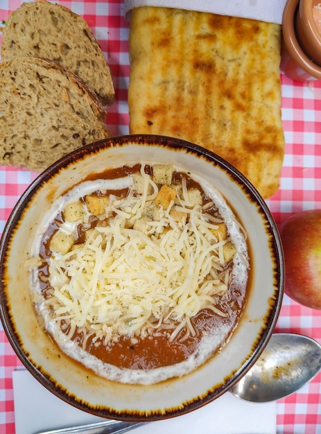 Un bol de soupe avec du fromage et du pain sur une table.