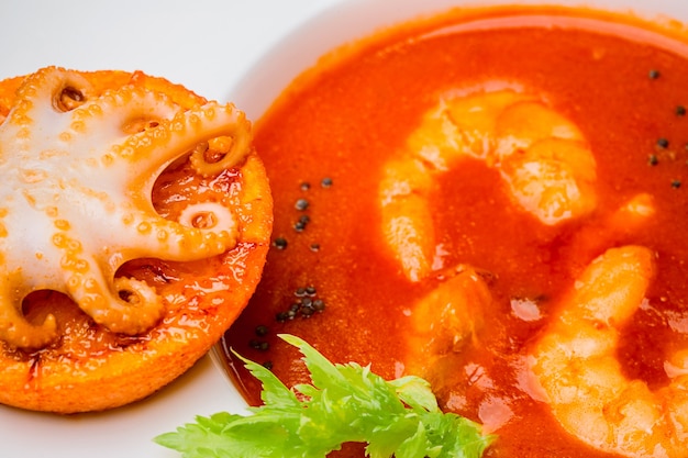 Bol de soupe de tomates aux crevettes avec une petite pieuvre cuite sur une tranche d'orange vue de dessus en gros plan