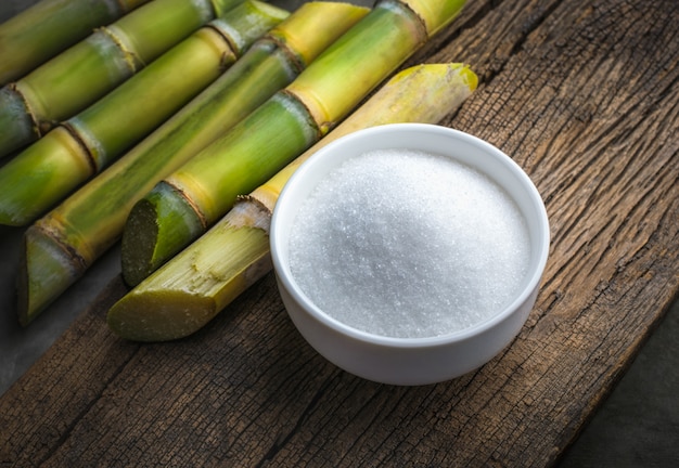 Bol de sucre blanc avec de la canne à sucre sur une table en bois.