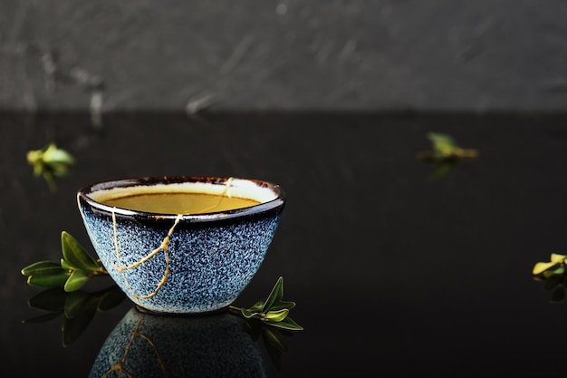 Bol à thé vert chaud, thé japonais sur fond sombre. Mise au point sélective sur la tasse. Tasse bleue en céramique récupérée, seconde vie des choses, recyclage
