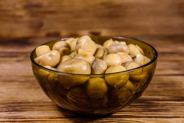 Bol en verre avec des champignons en conserve sur une table en bois rustique