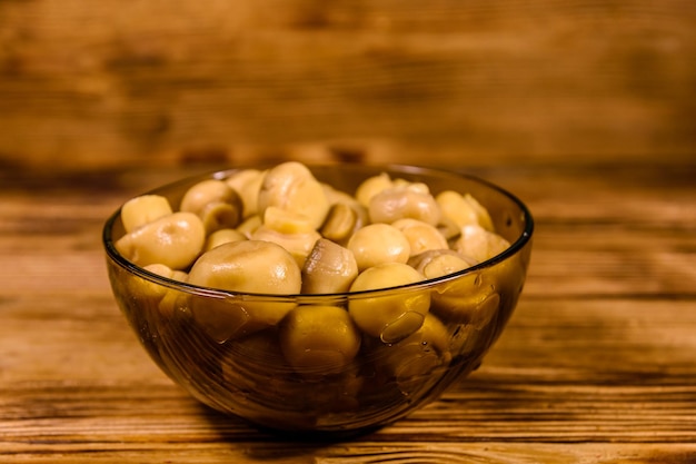 Bol en verre avec champignons en conserve sur table en bois