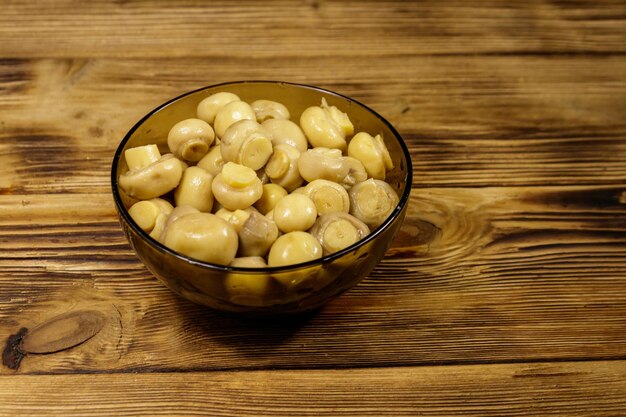 Bol en verre avec champignons marinés. Champignons marinés sur table en bois